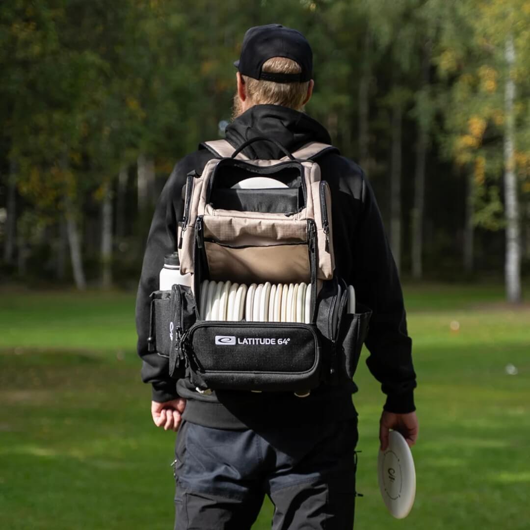 Player wearing the Latitude 64 DG Luxury E5 backpack in Sand/Black on the course